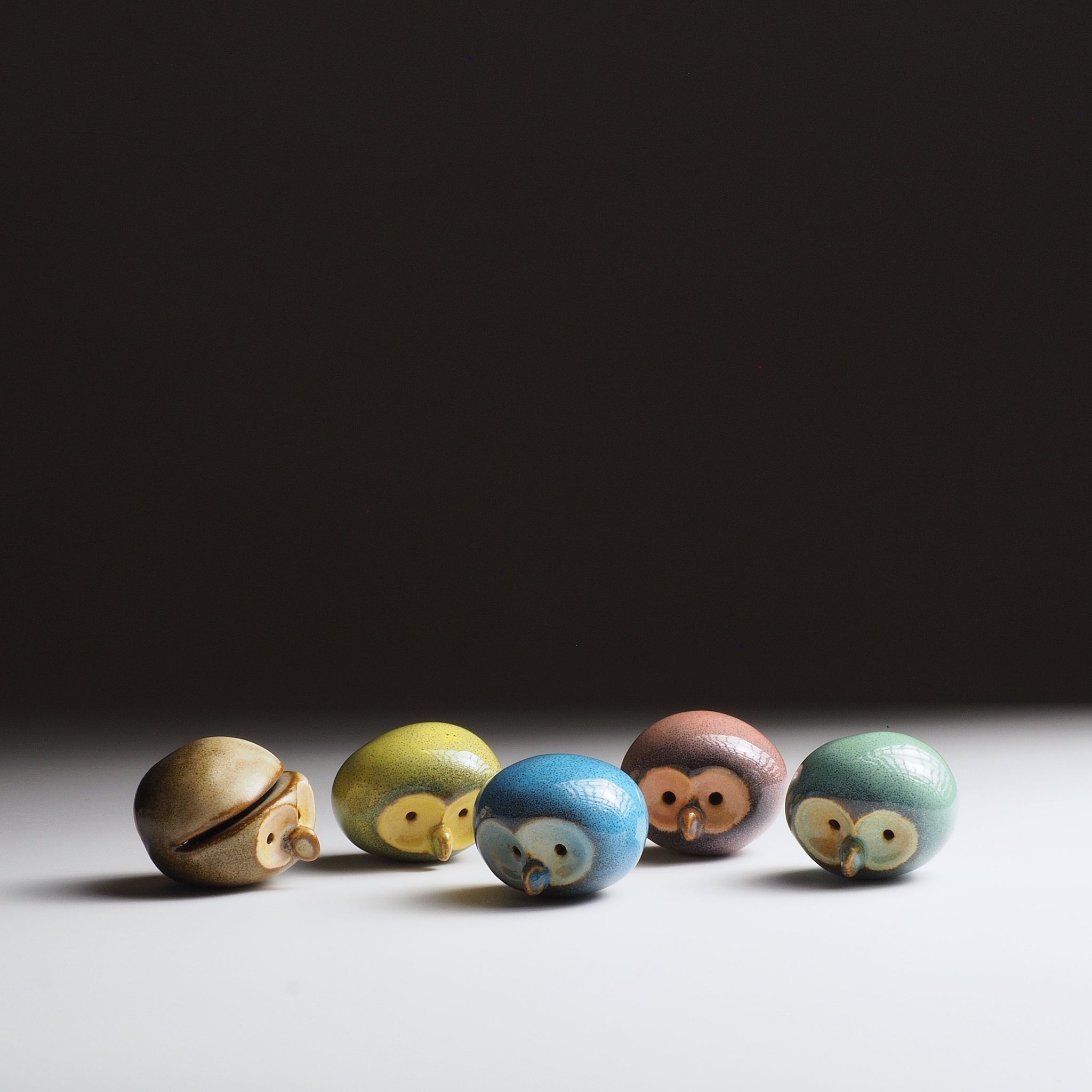 Top-down view of five Gofuku ceramic owl figurines showing gold-glazed faces and varied glaze colors. Handcrafted set.