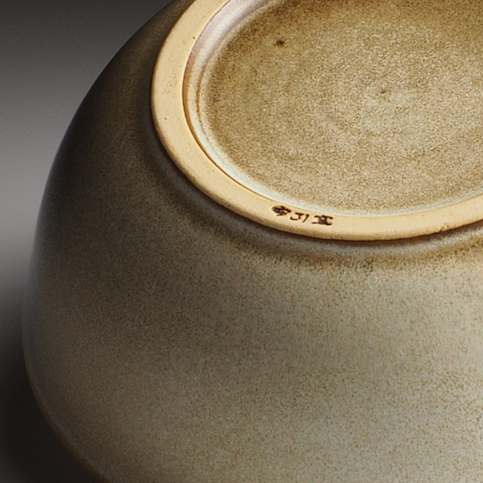 Foot close-up of a Japanese ceramic bowl with a visible brand logo on a dark background