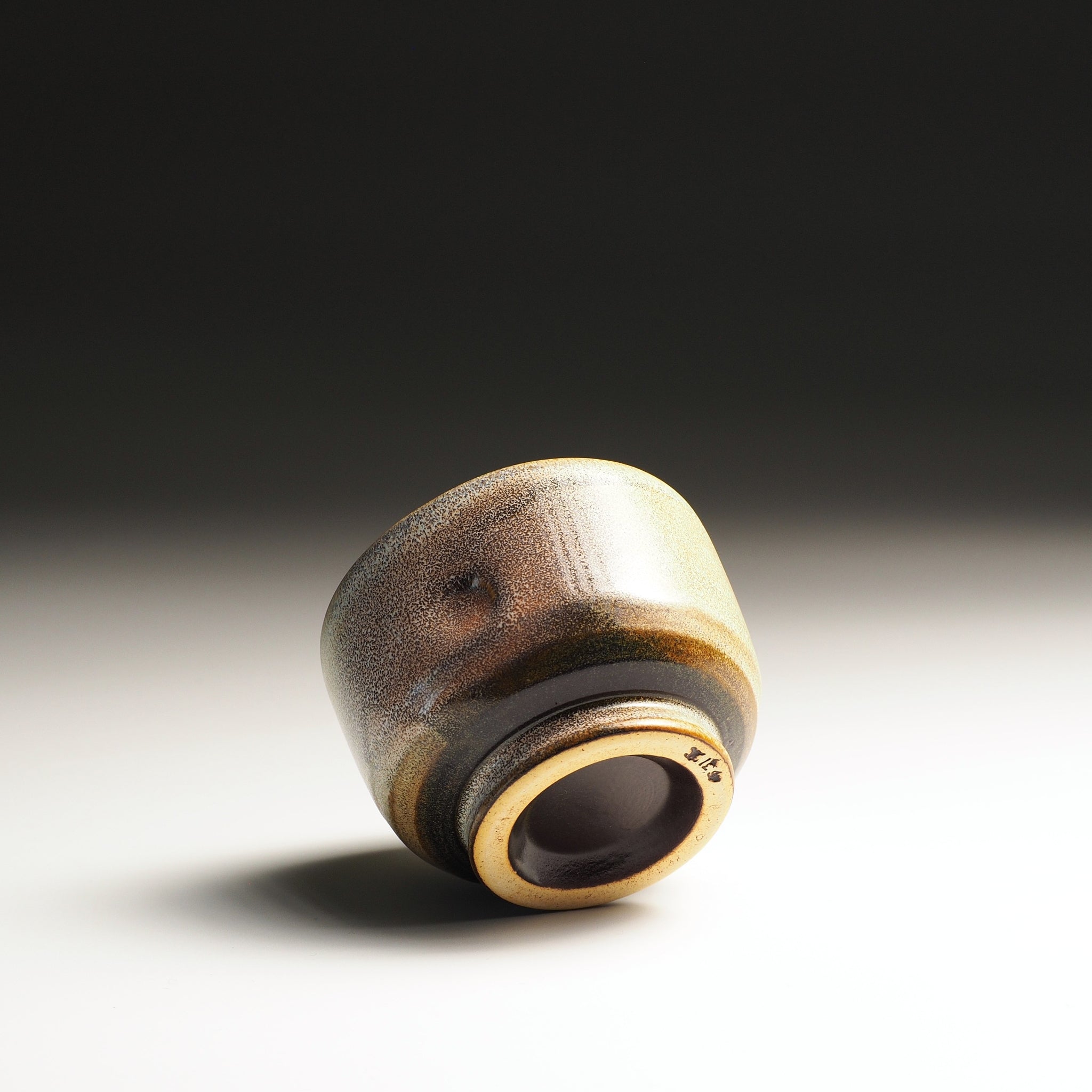 bottom view of a Japanese ceramic yunomi with brown and gold gradient on a dark background