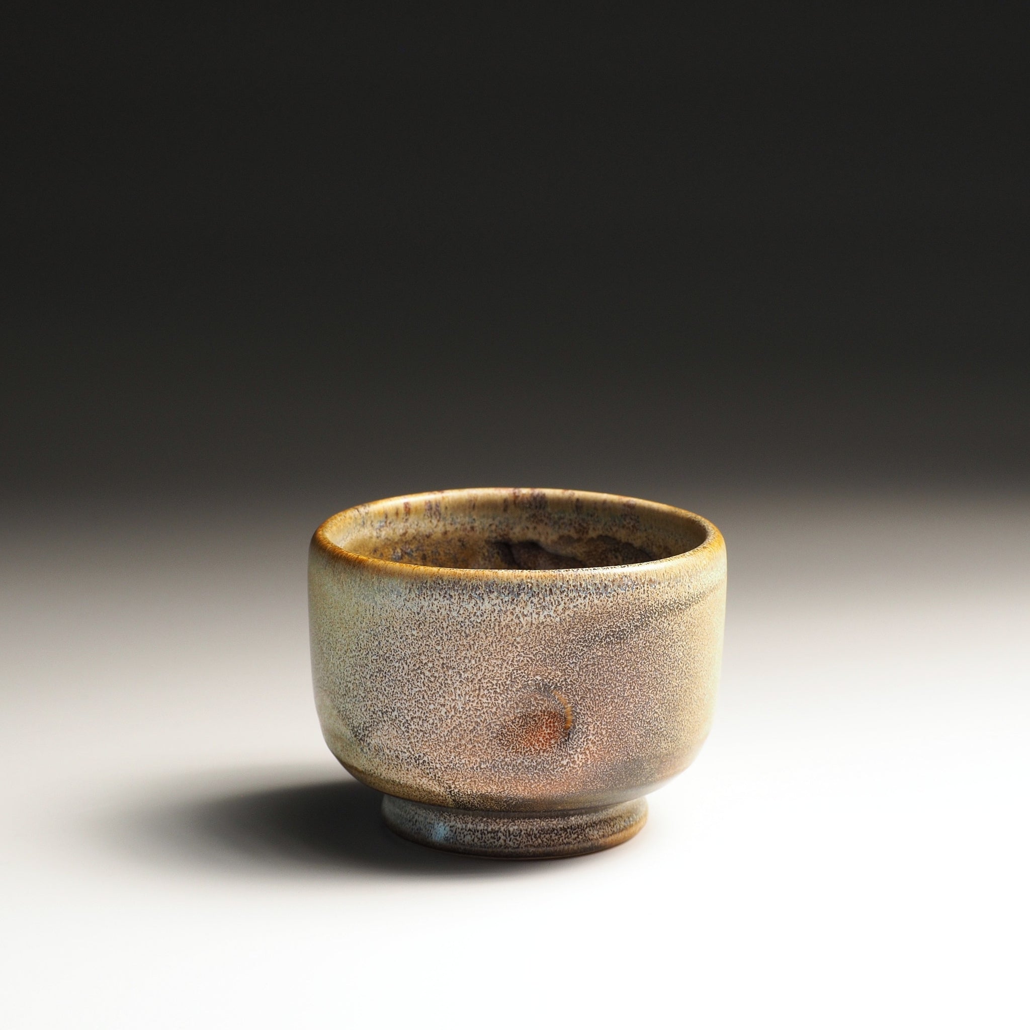 Small ceramic yunomi cup with a textured surface on a studio gradient background