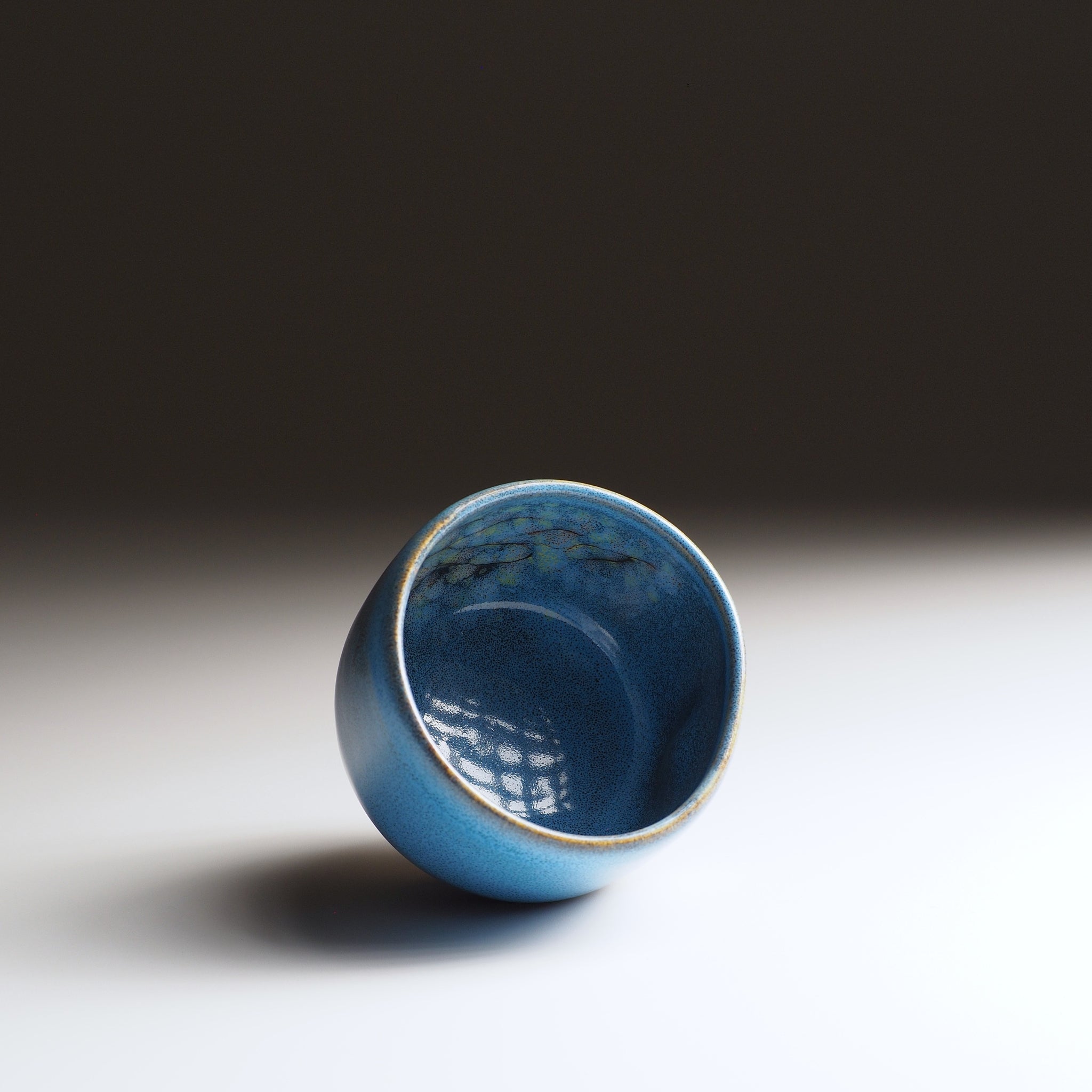 Oblique view of the Maru Komorebi Yunomi blue teacup, showing the inside decoration,  on a faded background.