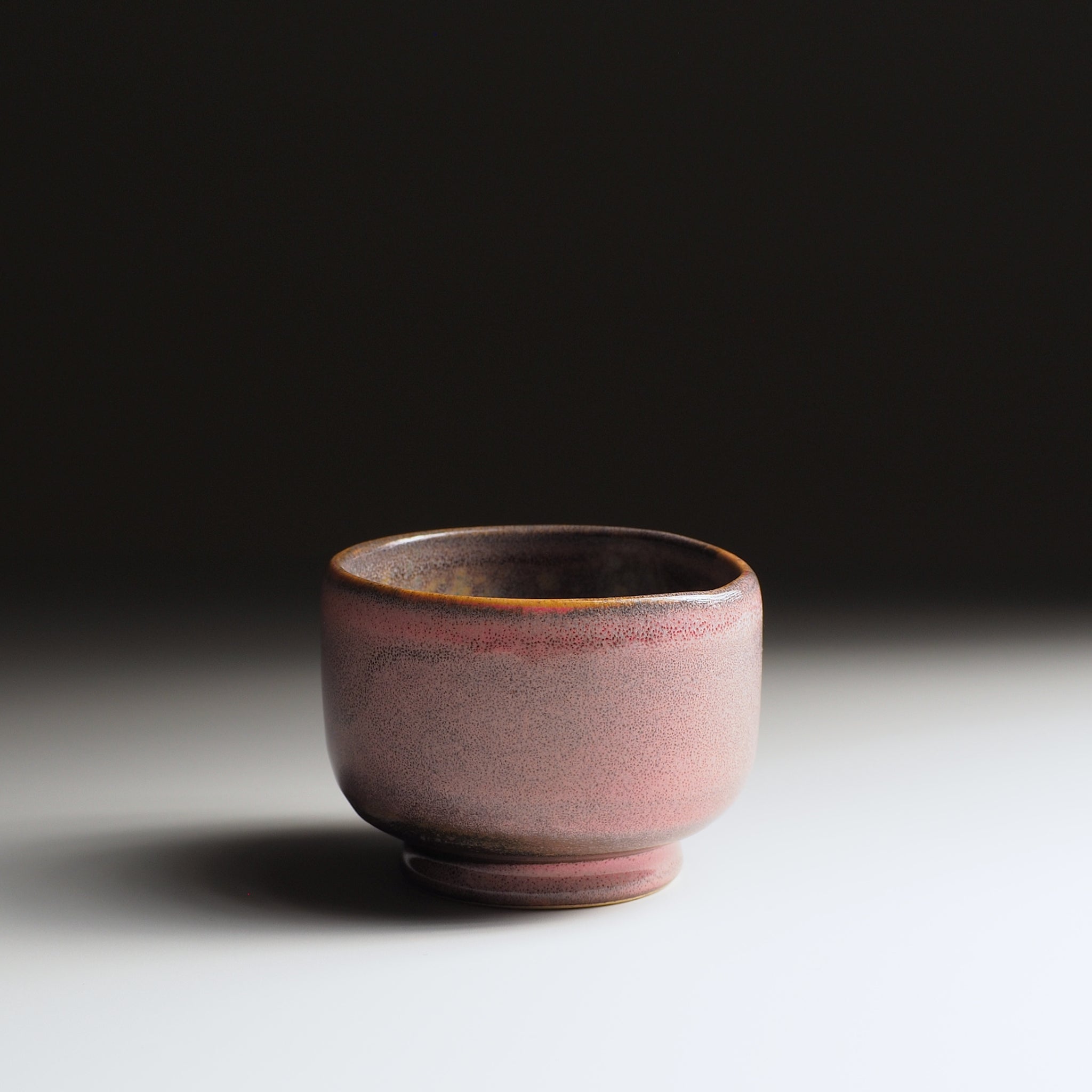 Japanese ceramic yunomi cup with a reddish-pink glaze on a dark background