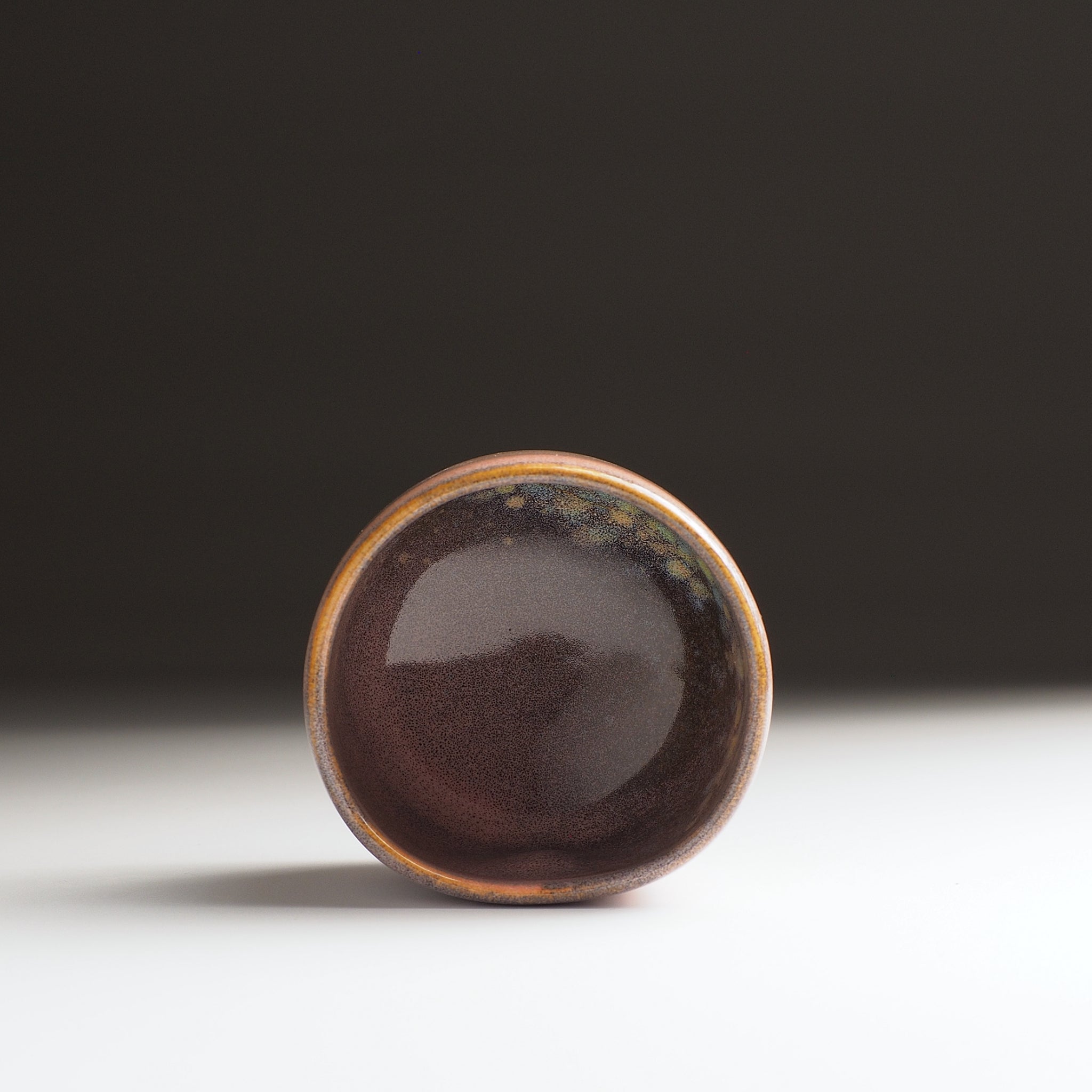 Interior view of a round ceramic yunomi teacup with a dark pink glaze on a white surface with a black background