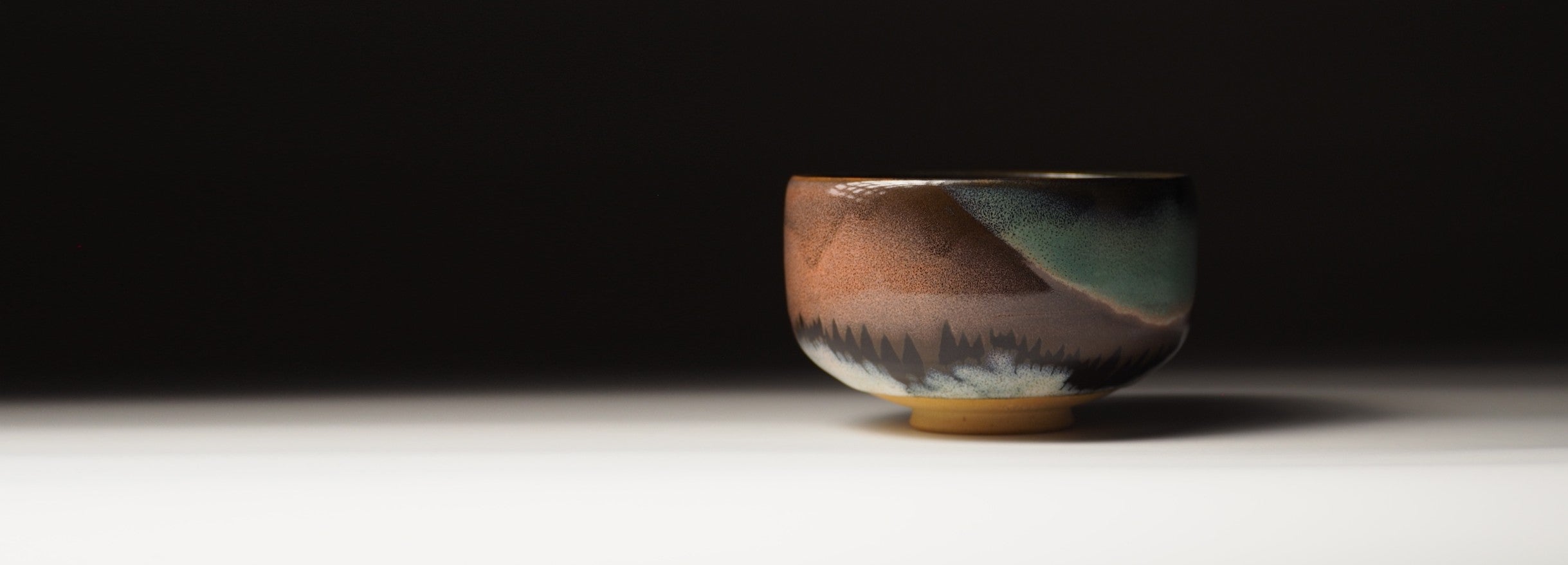 Ceramic matcha bowl with a scenic design on a dark background. Tsukushi