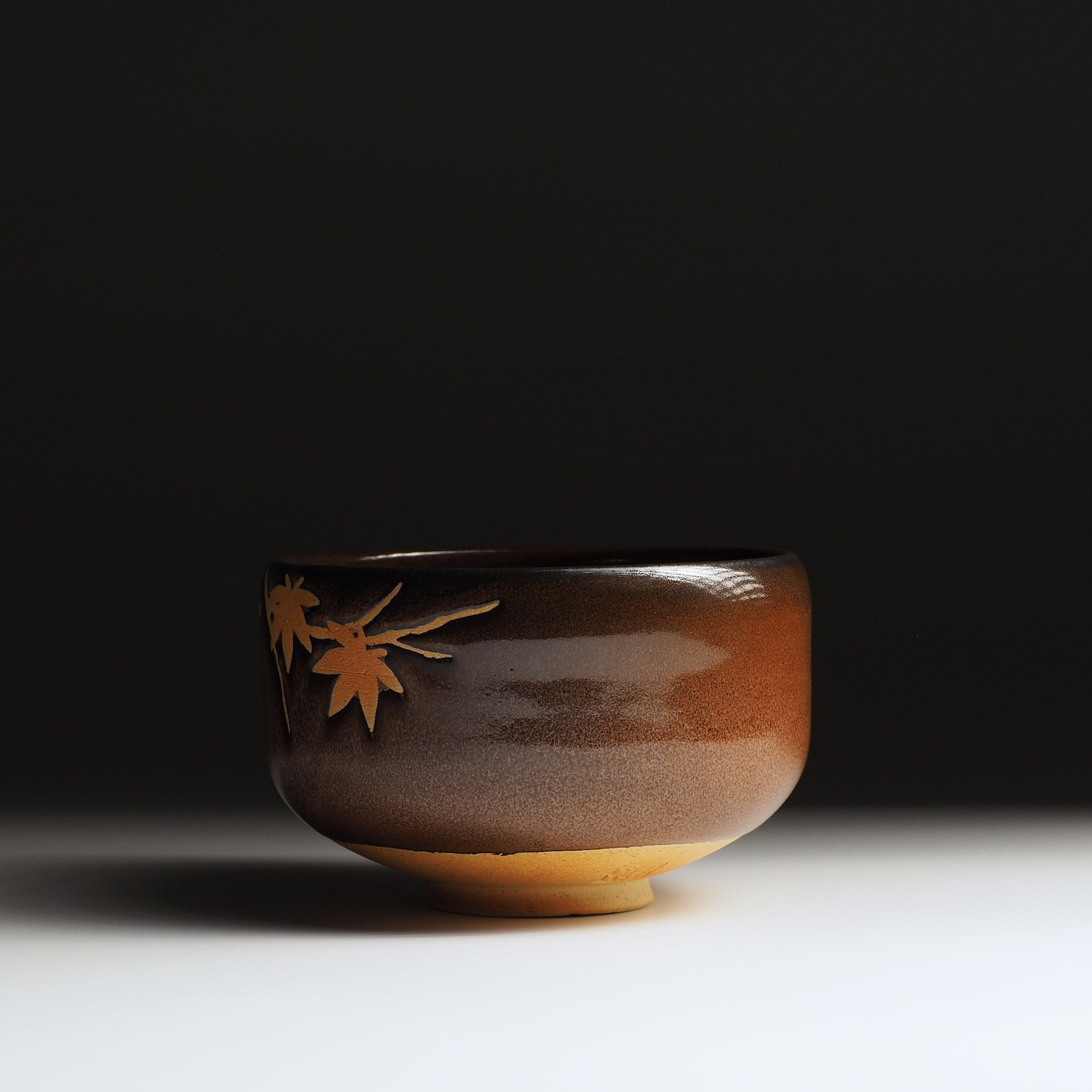 Yūkaede matcha bowl, side view highlighting Nanasai Tenmoku glaze gradation with small momiji sprig, Nunobiki Kiln